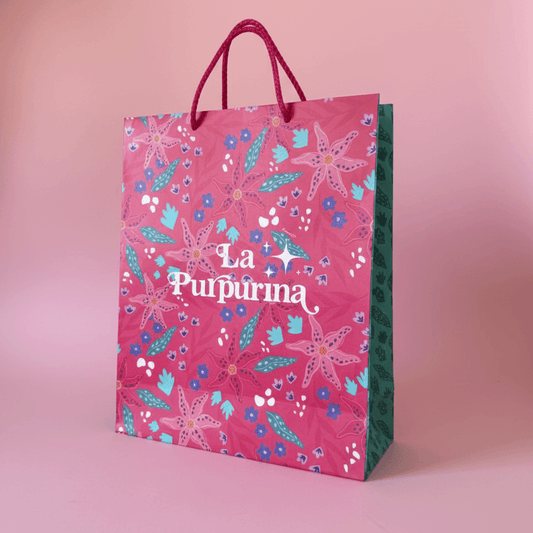 Bolsa para regalo La Purpurina con colorido diseño floral y asas rosas, perfecta para envolver regalos.